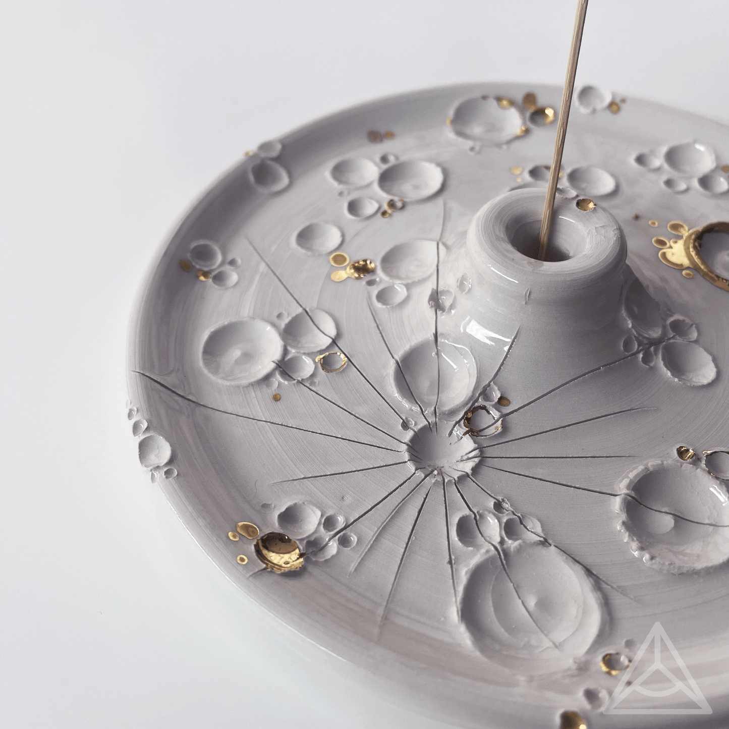 Primo piano di un porta-incenso in ceramica con finiture in oro lucido e un bastoncino di incenso, dettagli di design elegante su sfondo chiaro.