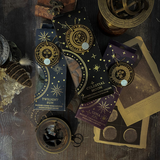 Assortimento di coni di incenso con supporto dalle fragranze celesti, ciascuno in una confezione tematica con motivi del Sole e della Luna, disposti artisticamente su un tavolo in legno, accanto a oggetti vintage e fiori secchi, evocando un'atmosfera di tranquillità e introspezione.