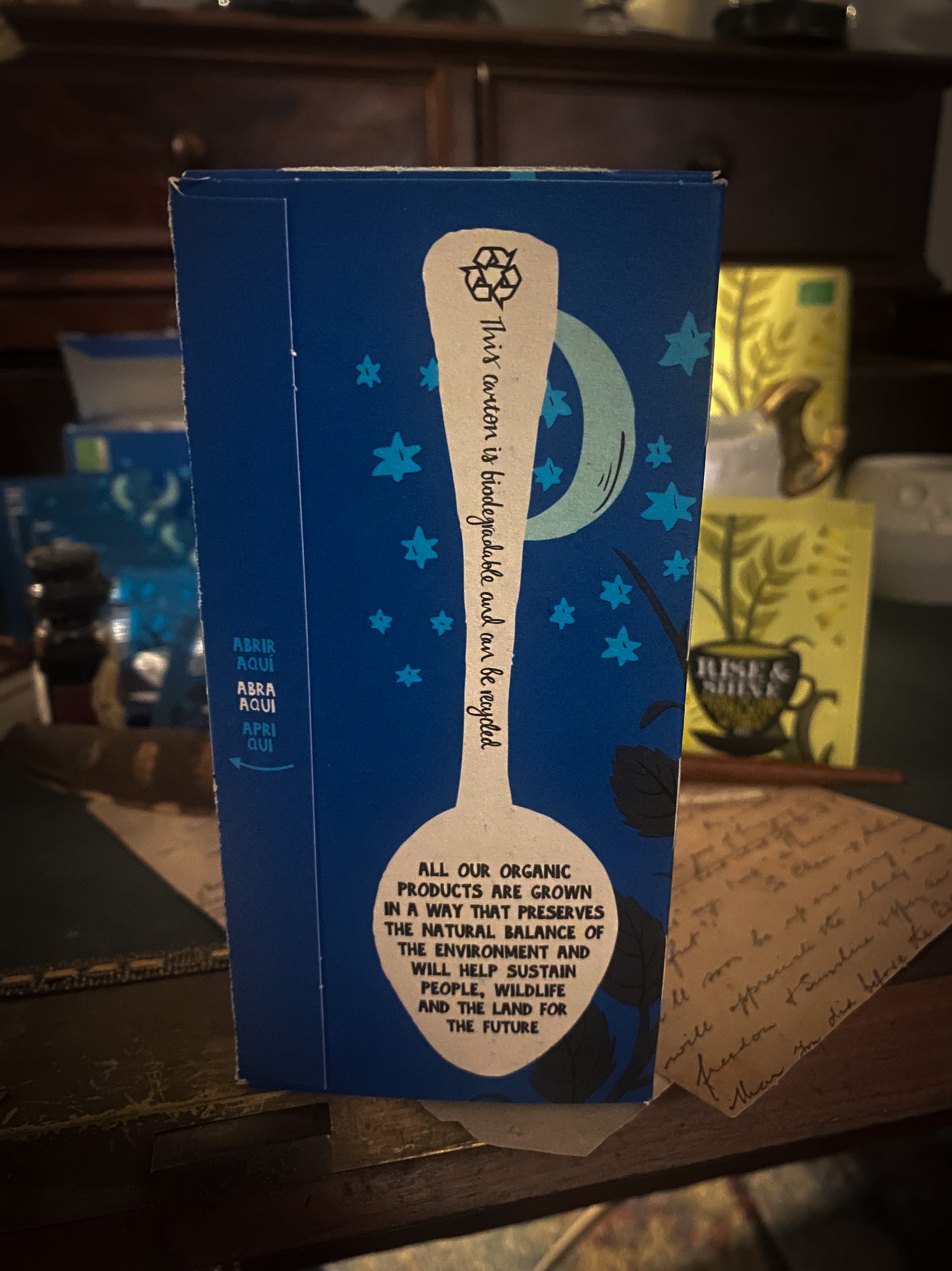 Un momento di relax con una tazza di tisana Cupper, circondata da pacchetti di tè vari assortiti, sullo sfondo di un'ambientazione accogliente con note scritte a mano e una penna stilografica, invitando a una pausa rilassante.
