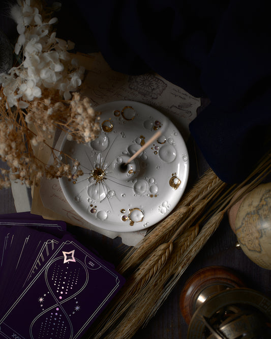 Atmosfera rilassante catturata con un porta-incenso in ceramica bianca e oro di ElaCeramics, incenso acceso e fumo serpeggiante che si innalza, su sfondo scuro.