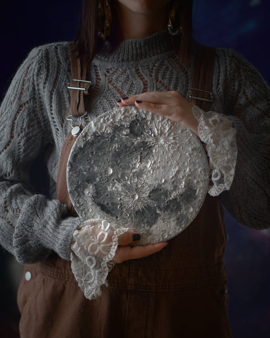 Una Luna in ceramica con crateri e riflessi argentati tenuta tra le mani