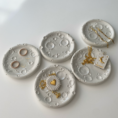Composizione artistica di porta-incensi in ceramica bianca, ciascuno con design unico, accompagnati da gioielli dorati e ambientazione luminosa.