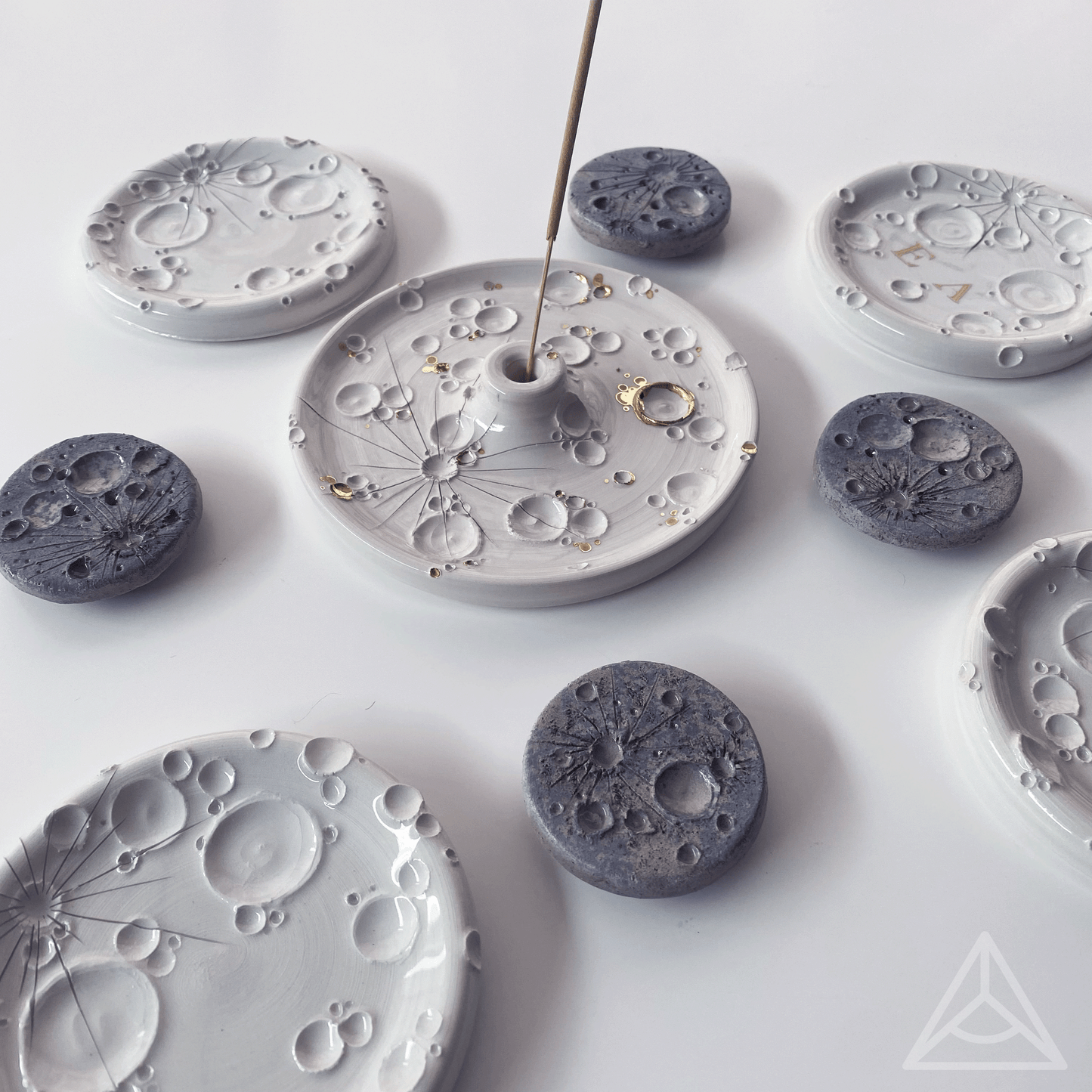 Collezione di porta-incensi in ceramica con vari disegni e texture, con bastoncini di incenso inseriti, su sfondo bianco.