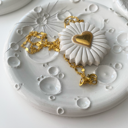 Portagioie in ceramica bianca con dettagli dorati, presentando un elegante braccialetto e una collana appoggiati su di esso, in una composizione pura e sofisticata.