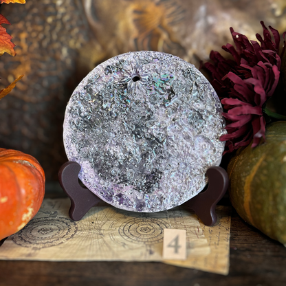 Luna della Soglia IV, luna media in ceramica viola su un leggio con il numero 4, fra zucche e fiori scuri
