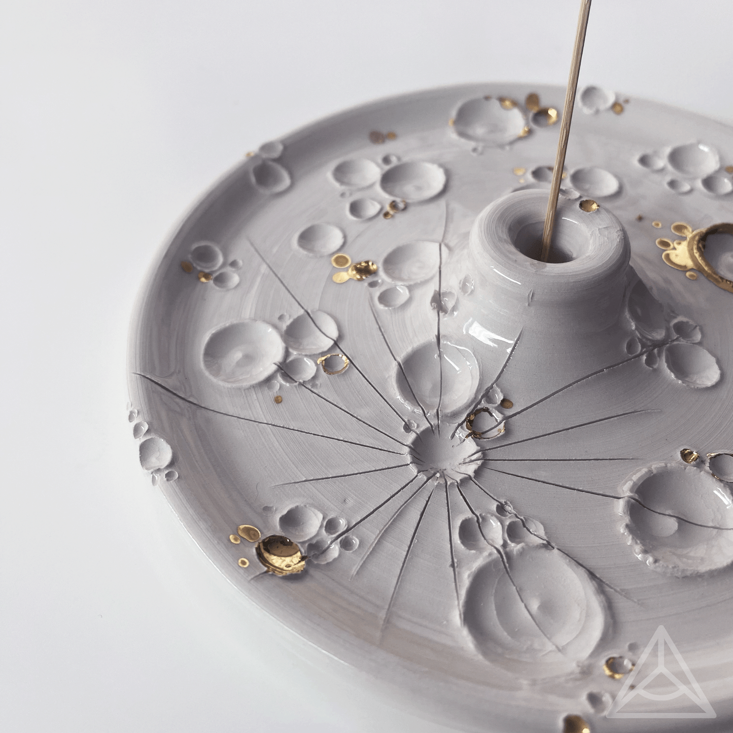 Primo piano di un porta-incenso in ceramica con finiture in oro lucido e un bastoncino di incenso, dettagli di design elegante su sfondo chiaro.