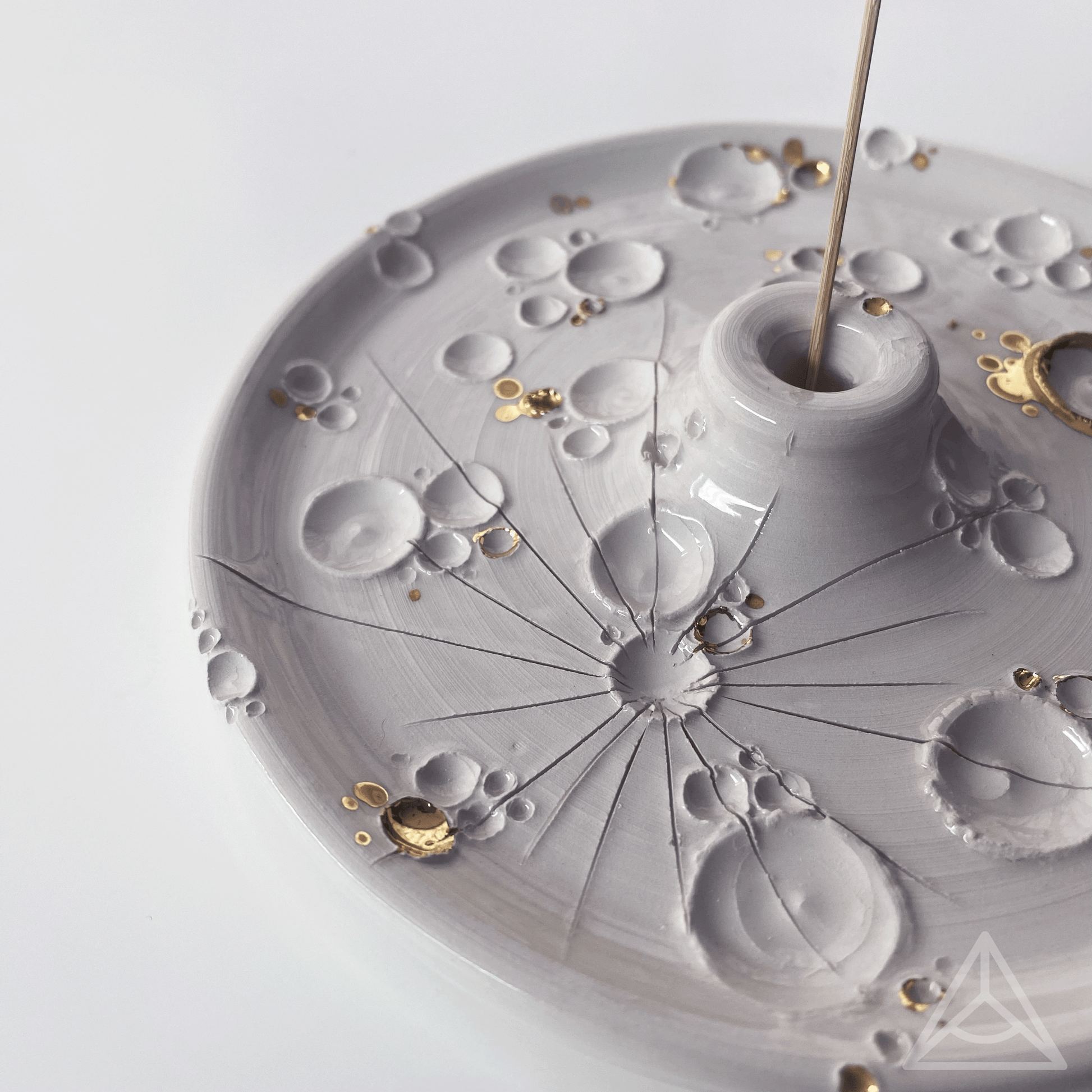 Primo piano di un porta-incenso in ceramica con finiture in oro lucido e un bastoncino di incenso, dettagli di design elegante su sfondo chiaro.