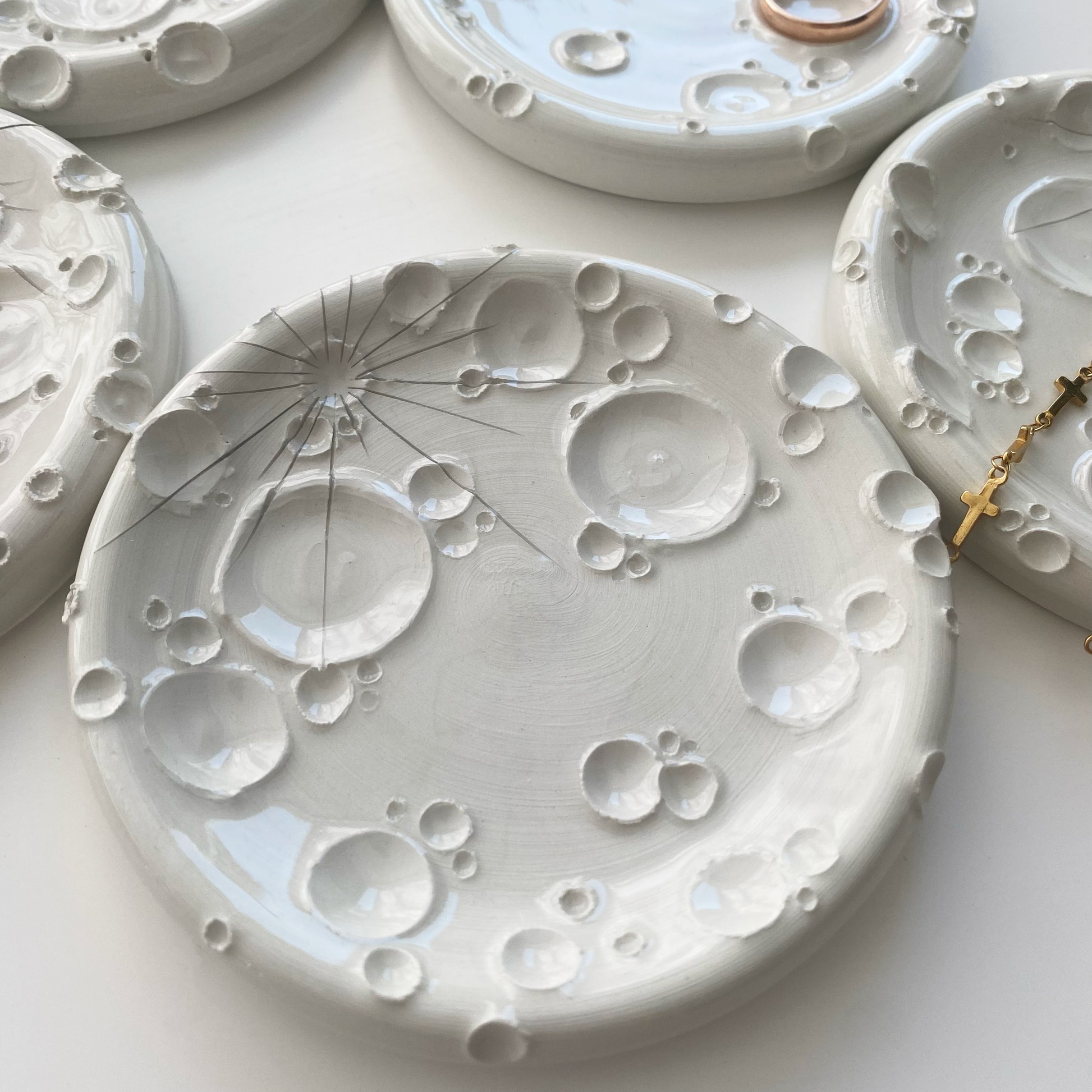 Composizione artistica di porta-incensi in ceramica bianca, ciascuno con design unico, accompagnati da gioielli dorati e ambientazione luminosa.