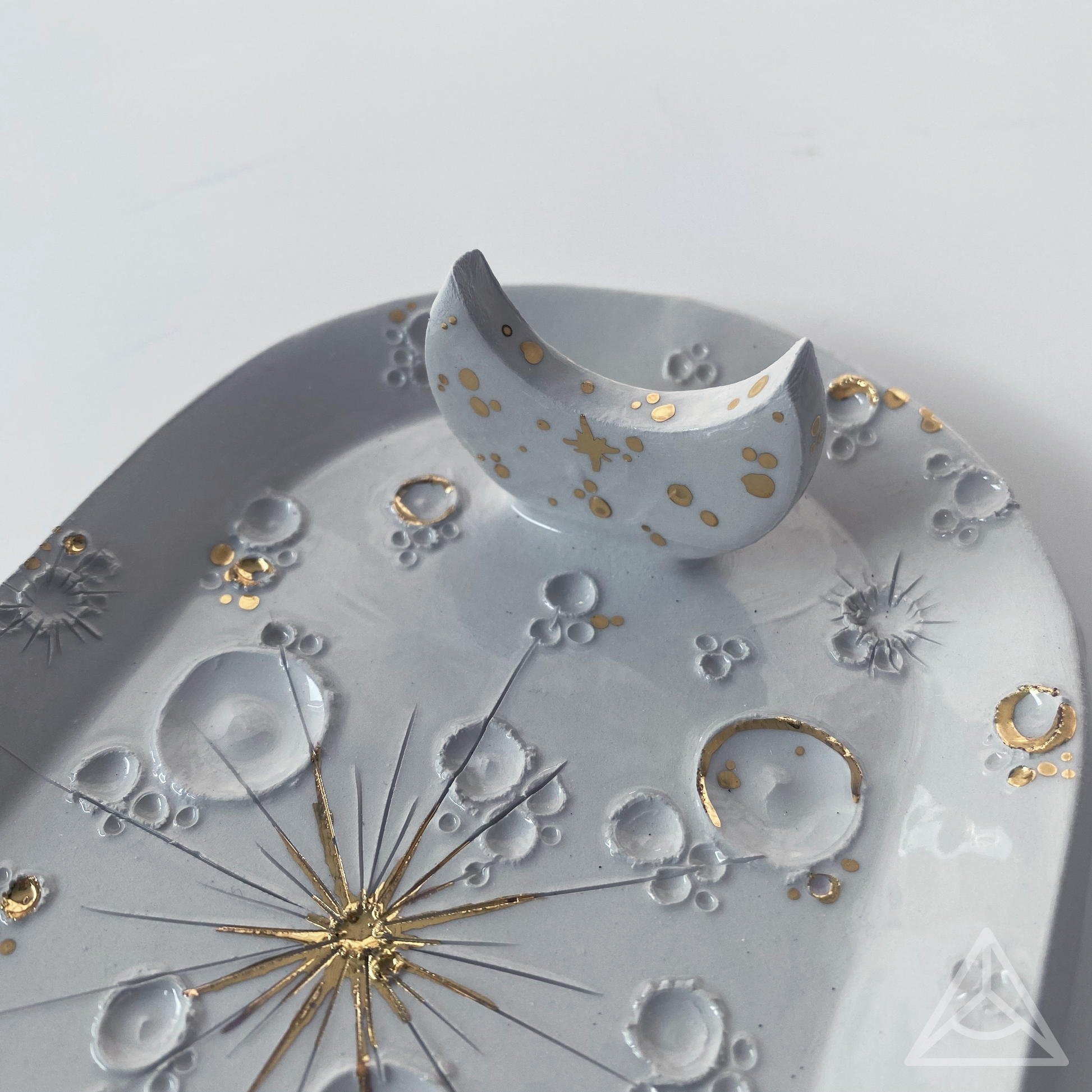 Vista ravvicinata di un porta-incenso in ceramica bianca decorato con elementi d'oro, con diverse fasi lunari.