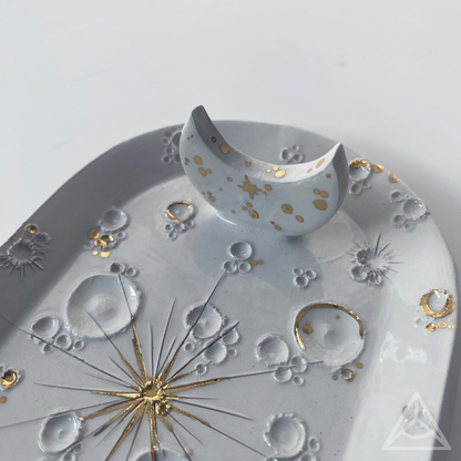 Vista ravvicinata di un porta-incenso in ceramica bianca decorato con elementi d'oro, con diverse fasi lunari.