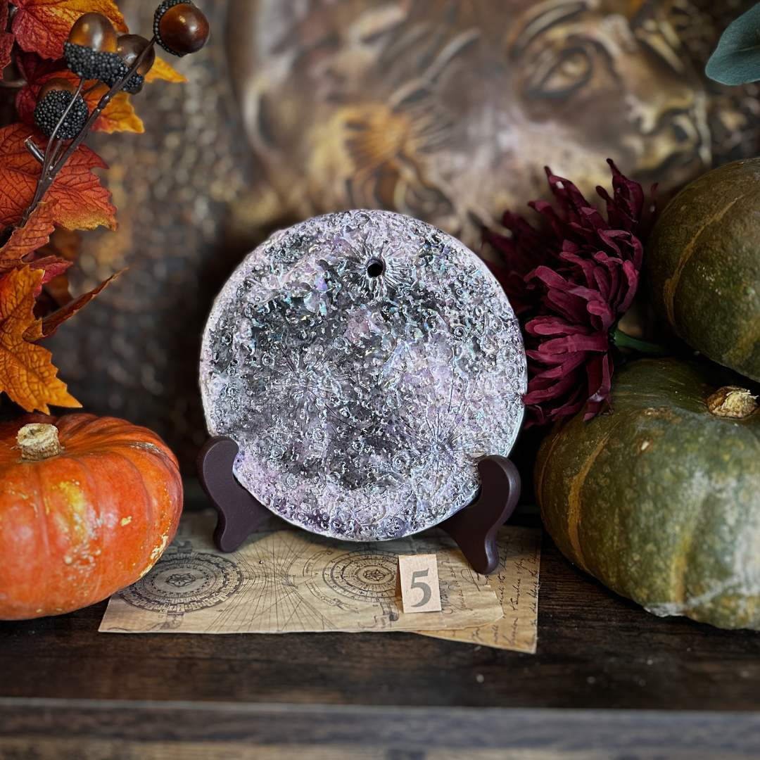 Luna della Soglia V, luna media in ceramica viola su un leggio con il numero 5, fra le zucche