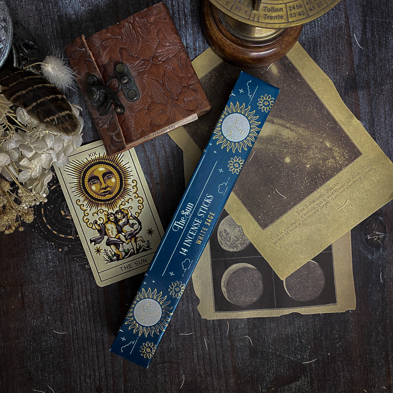 Bastoncini d'incenso esoterici con temi astrali e simboli dei tarocchi, come La Luna e La Stella, disposti artisticamente su un tavolo scuro con sfondo di oggetti vintage e botanica essiccata