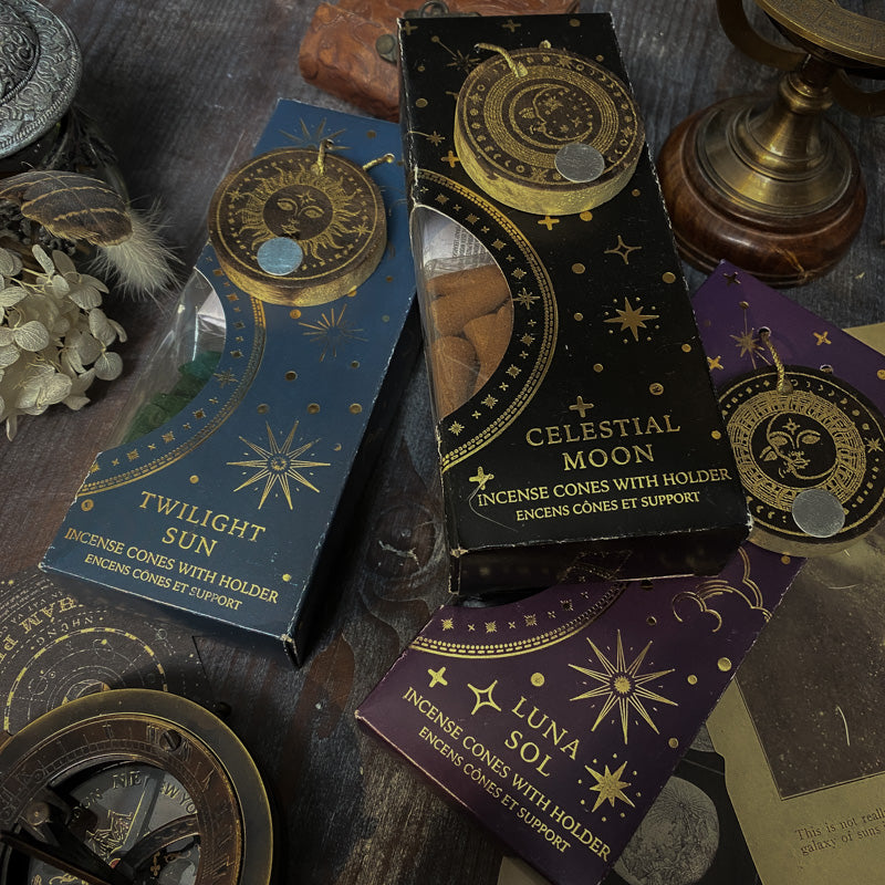 Assortimento di coni di incenso con supporto dalle fragranze celesti, ciascuno in una confezione tematica con motivi del Sole e della Luna, disposti artisticamente su un tavolo in legno, accanto a oggetti vintage e fiori secchi, evocando un'atmosfera di tranquillità e introspezione.