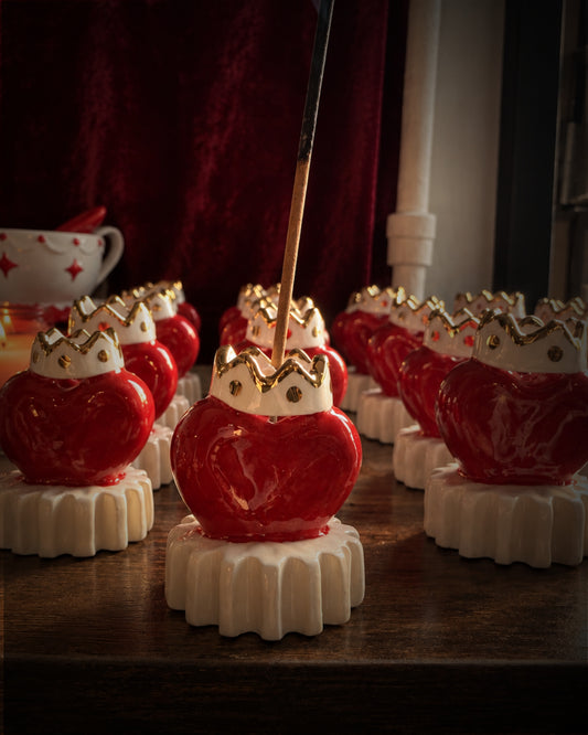 Porta incenso a cuore Breathe Me in ceramica rossa con corona in oro, allineati su un tavolo di legno scuro