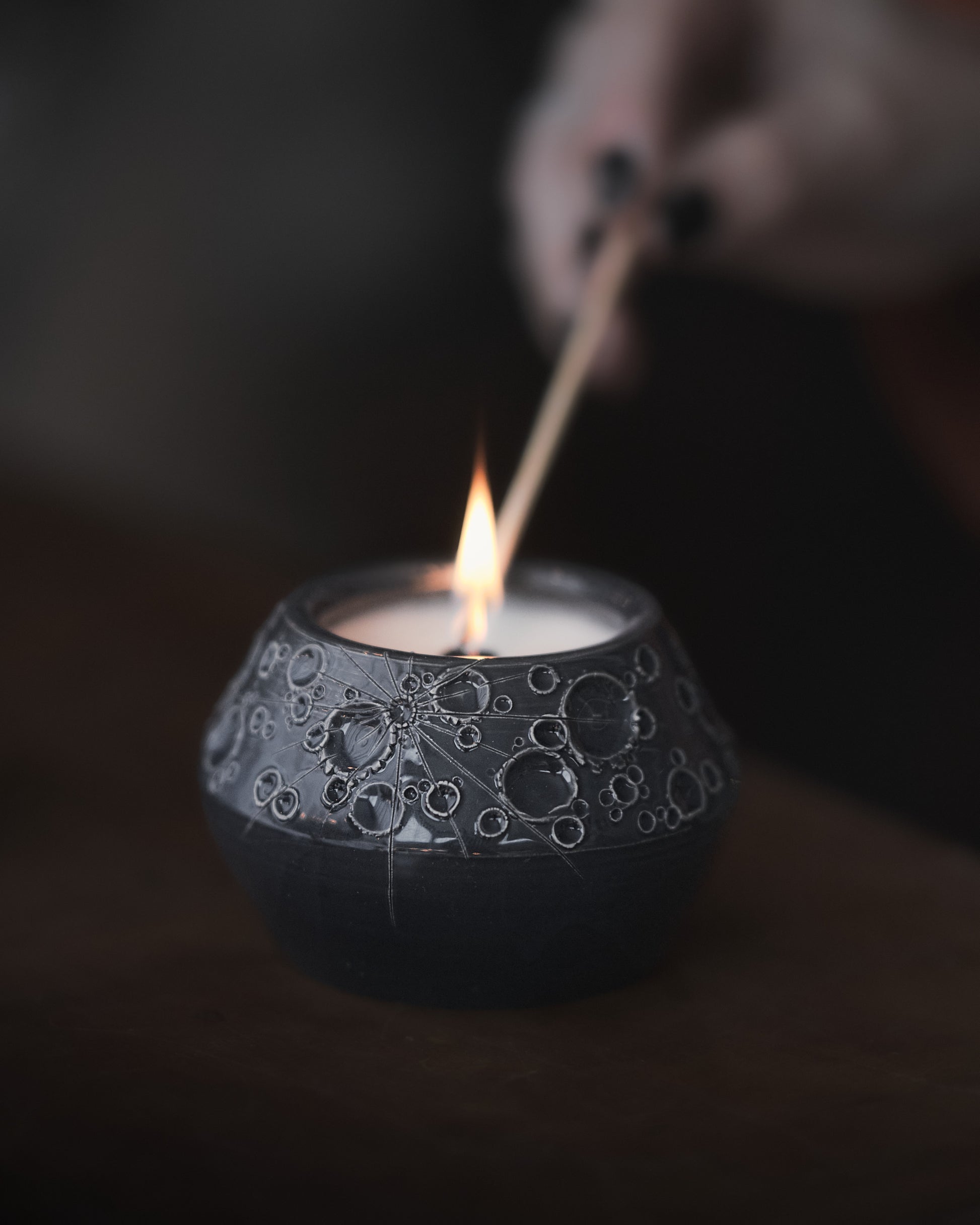 mano che accende una candela lunare artigianale nera fatta a mano