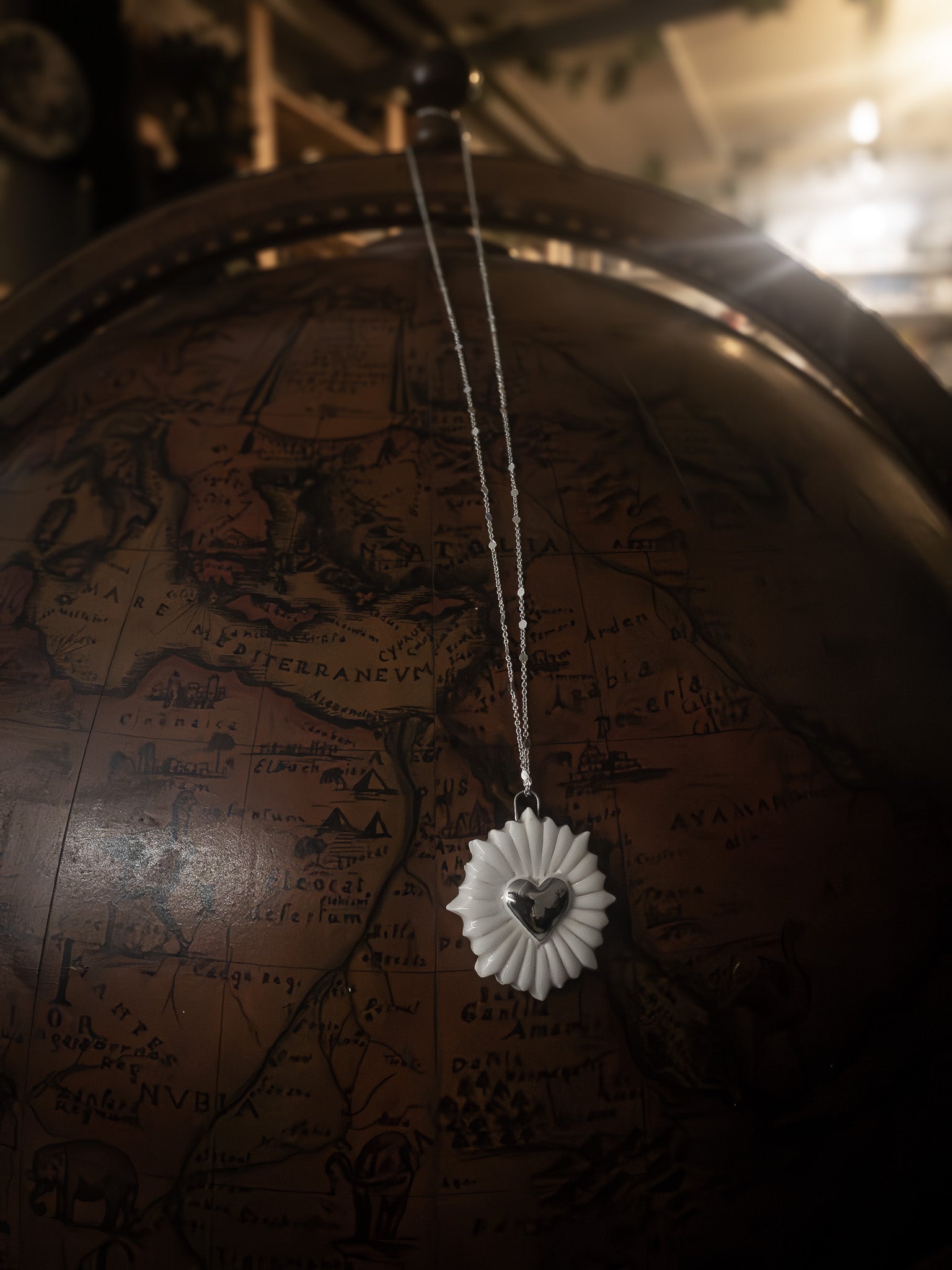 collana a forma di cuore sacro con cuore in platino appesa su un mappamondo vintage