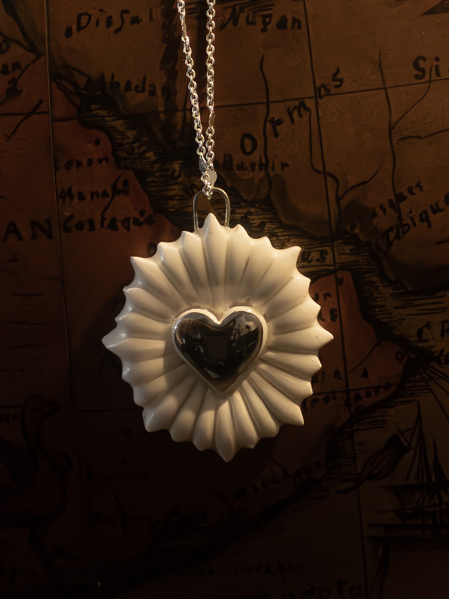 ravvicinato collana a forma di cuore sacro con cuore in platino appesa su un mappamondo vintage