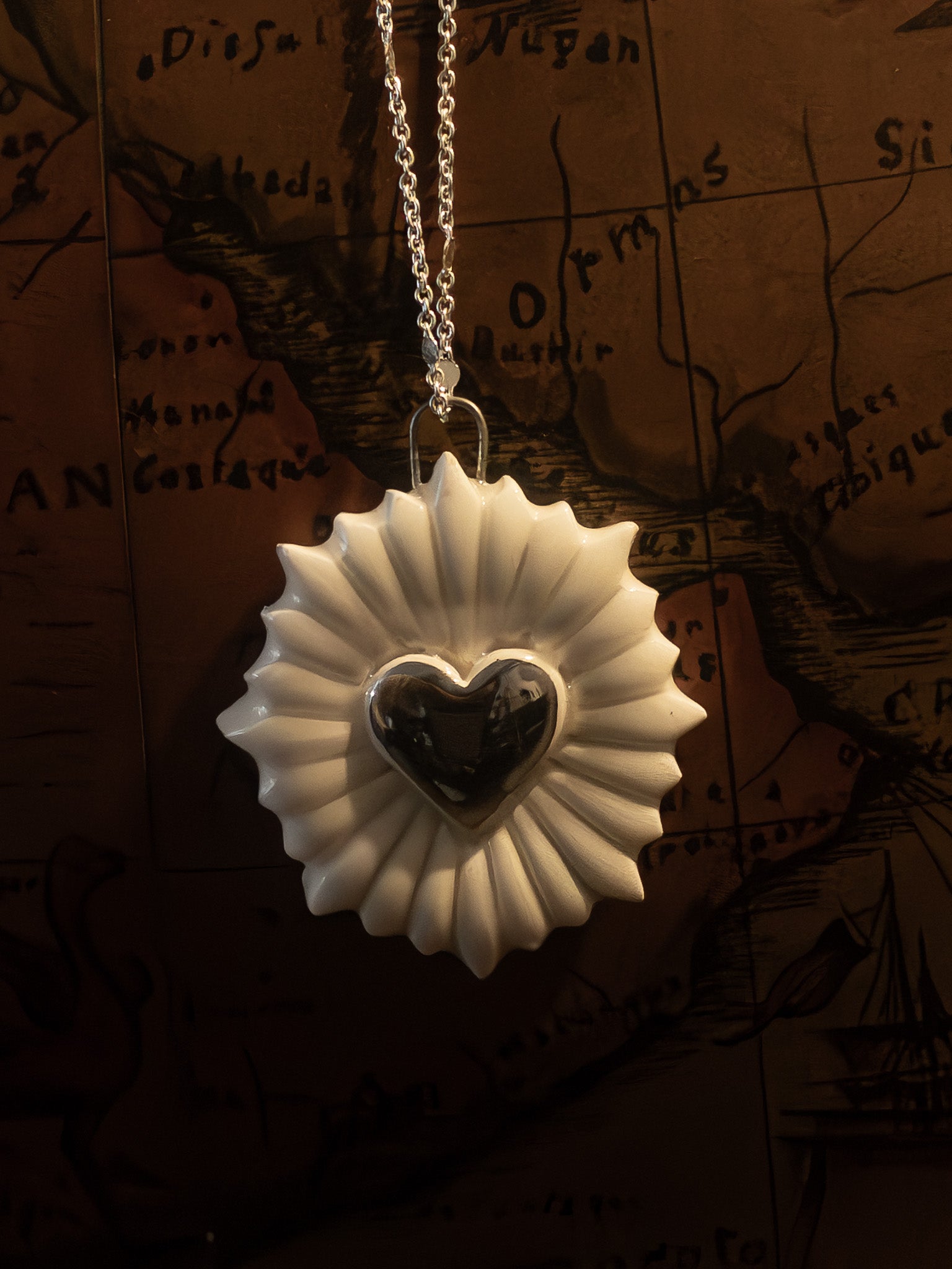 ravvicinato collana a forma di cuore sacro con cuore in platino appesa su un mappamondo vintage