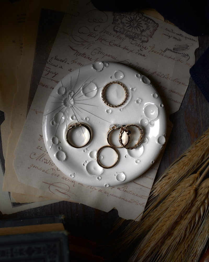 Vista dall'alto di un portagioie e porta-incenso bianco con finiture in oro, abbellito con anelli dorati, posato su pagine calligrafiche, che evoca un senso di eleganza e tradizione.