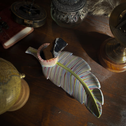 Un portaincenso artistico in ceramica a forma di foglia con una barretta di palo santo, disposto su un tavolo scuro con oggetti vintage come un diario in pelle, un astrolabio e un globo.