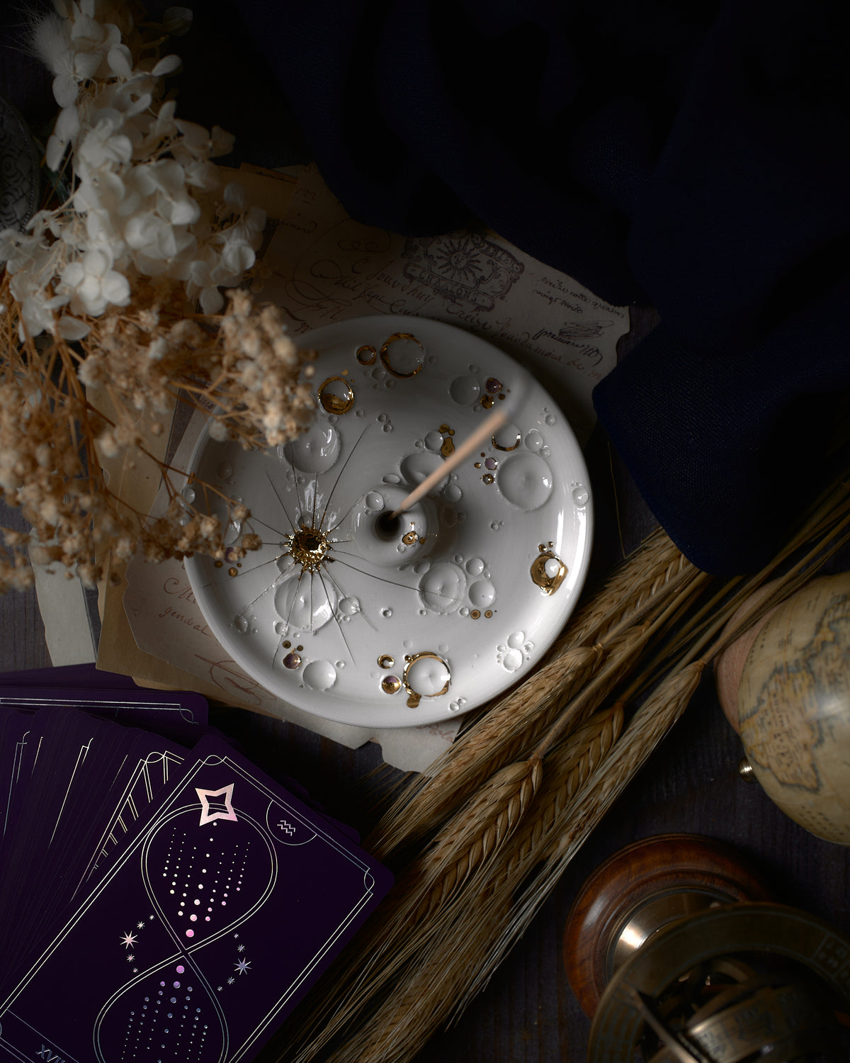 Atmosfera rilassante catturata con un porta-incenso in ceramica bianca e oro di ElaCeramics, incenso acceso e fumo serpeggiante che si innalza, su sfondo scuro.