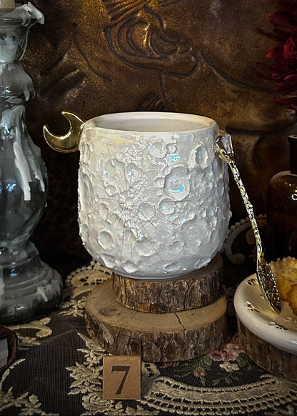 Tazza lunare 7 in ceramica su supporto in legno, tra candela, pizzo e biscotti