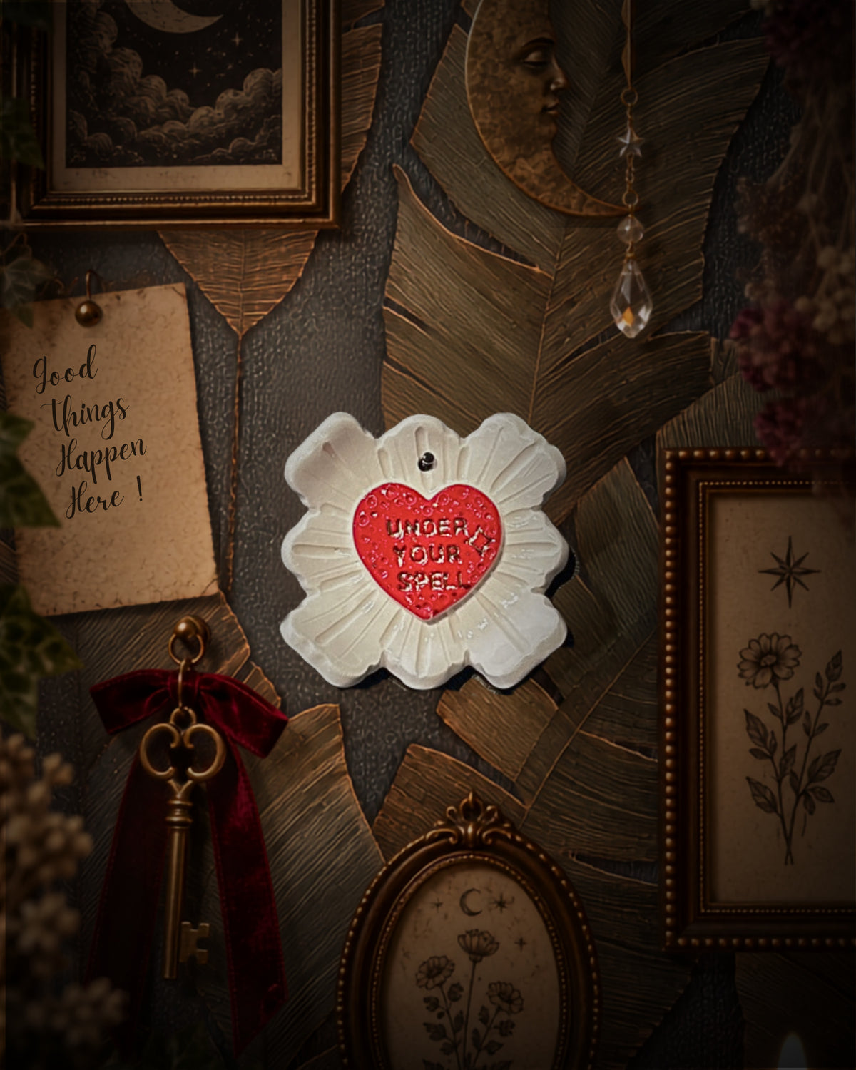 Quadretto Under Your Spell in ceramica bianca con cuore rosso e scritta in oro, appeso a una parete di cornici