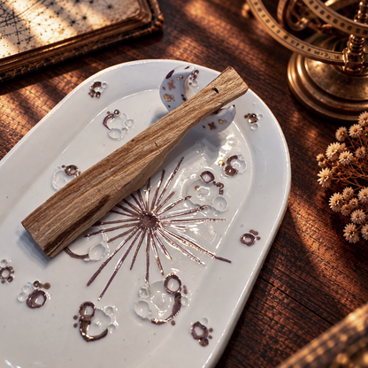 Dettaglio del piattino White and Rose Gold con crateri, raggi in lustro oro rosa e palo santo appoggiato alla mezzaluna.