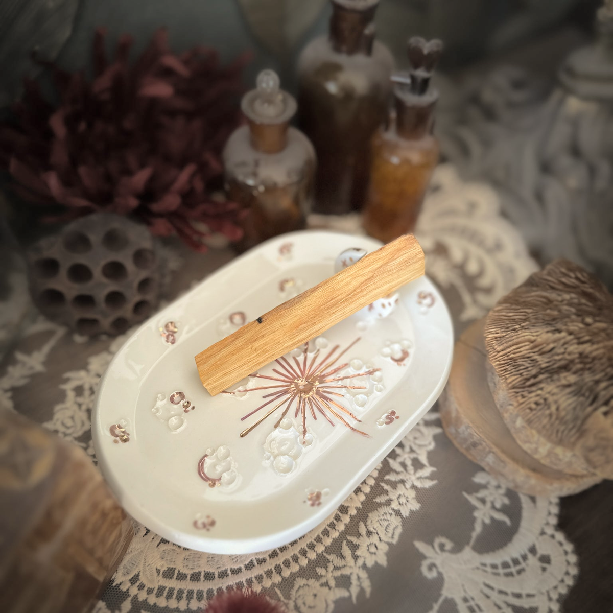 Piattino lunare White and Rose Gold con palo santo, su pizzo e legno tra fiori secchi e boccette vintage.