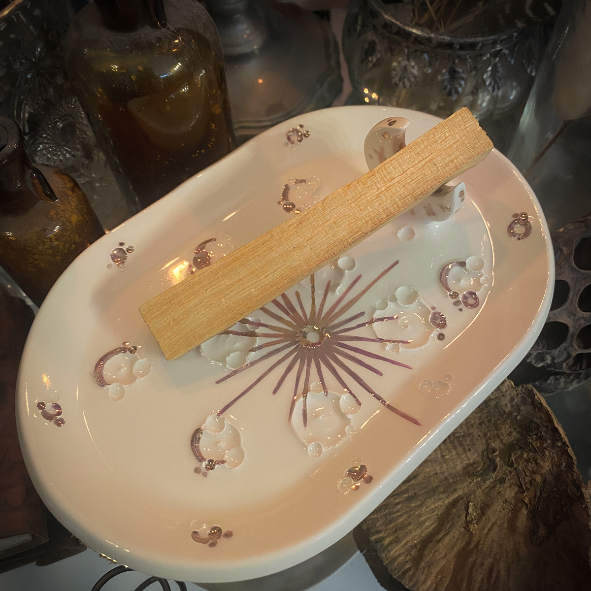 Dettaglio del piattino in ceramica bianca e oro rosa con palo santo appoggiato alla mezzaluna.
